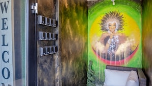 Una habitación con un cartel de 'WELCOME', una cama, una mesita pequeña y un mural en la pared.