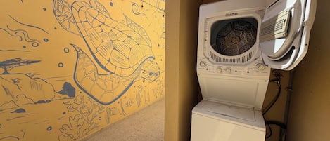 Un mur orné d’une fresque et sur lequel est adossée une machine à laver blanche.