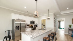 A modern kitchen with white cabinets, stainless steel appliances, granite countertops, and bar stools. - 2 Free Kayaks! Gorgeous Home with Great Lakefront Outdoor Space (Mabank)