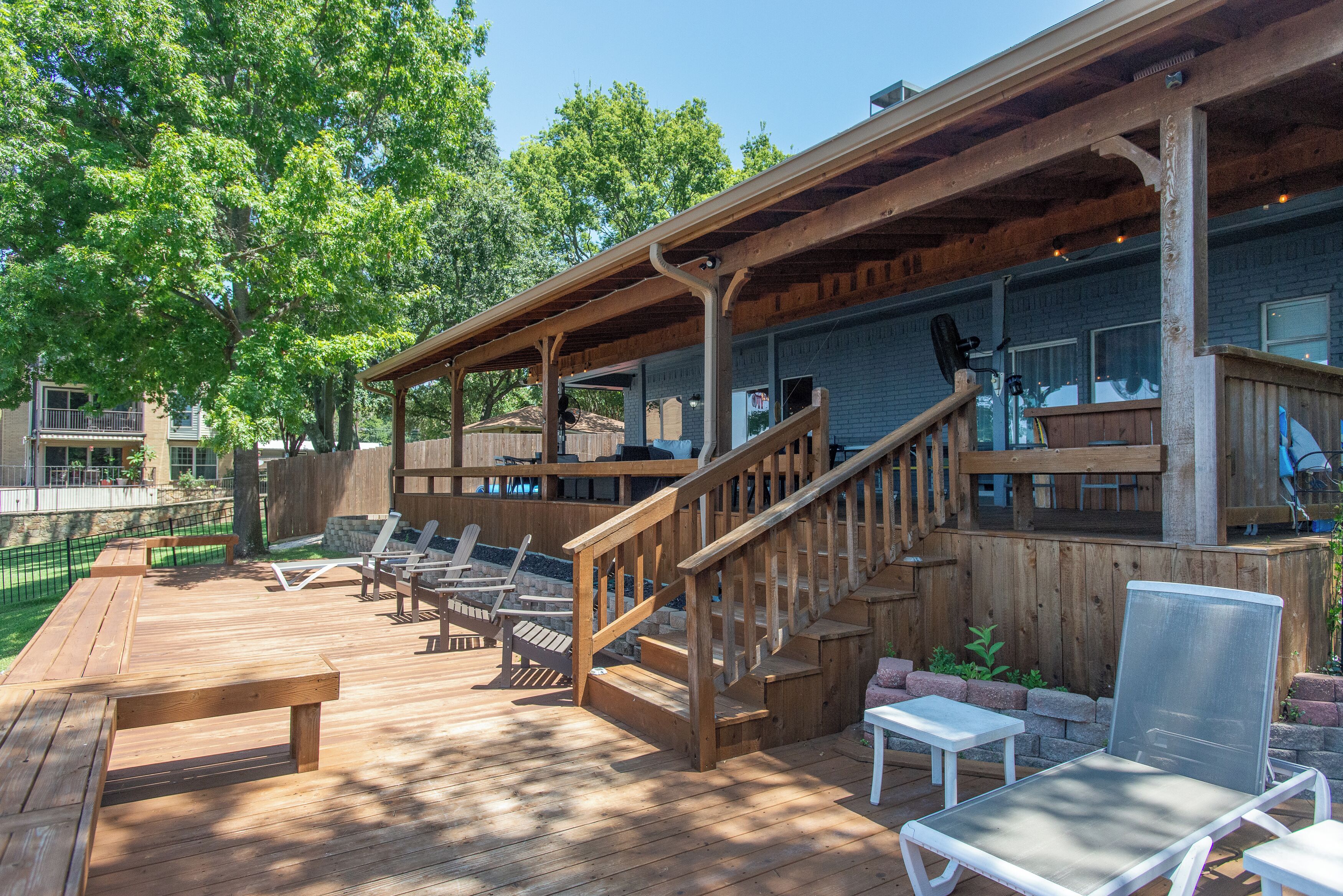 Une terrasse en bois avec des chaises longues et un espace salon couvert, accessible par un escalier.