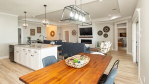 A modern kitchen with white cabinets, a wooden dining table, and a hanging light fixture. - 2 Free Kayaks! Gorgeous Home with Great Lakefront Outdoor Space (Mabank)