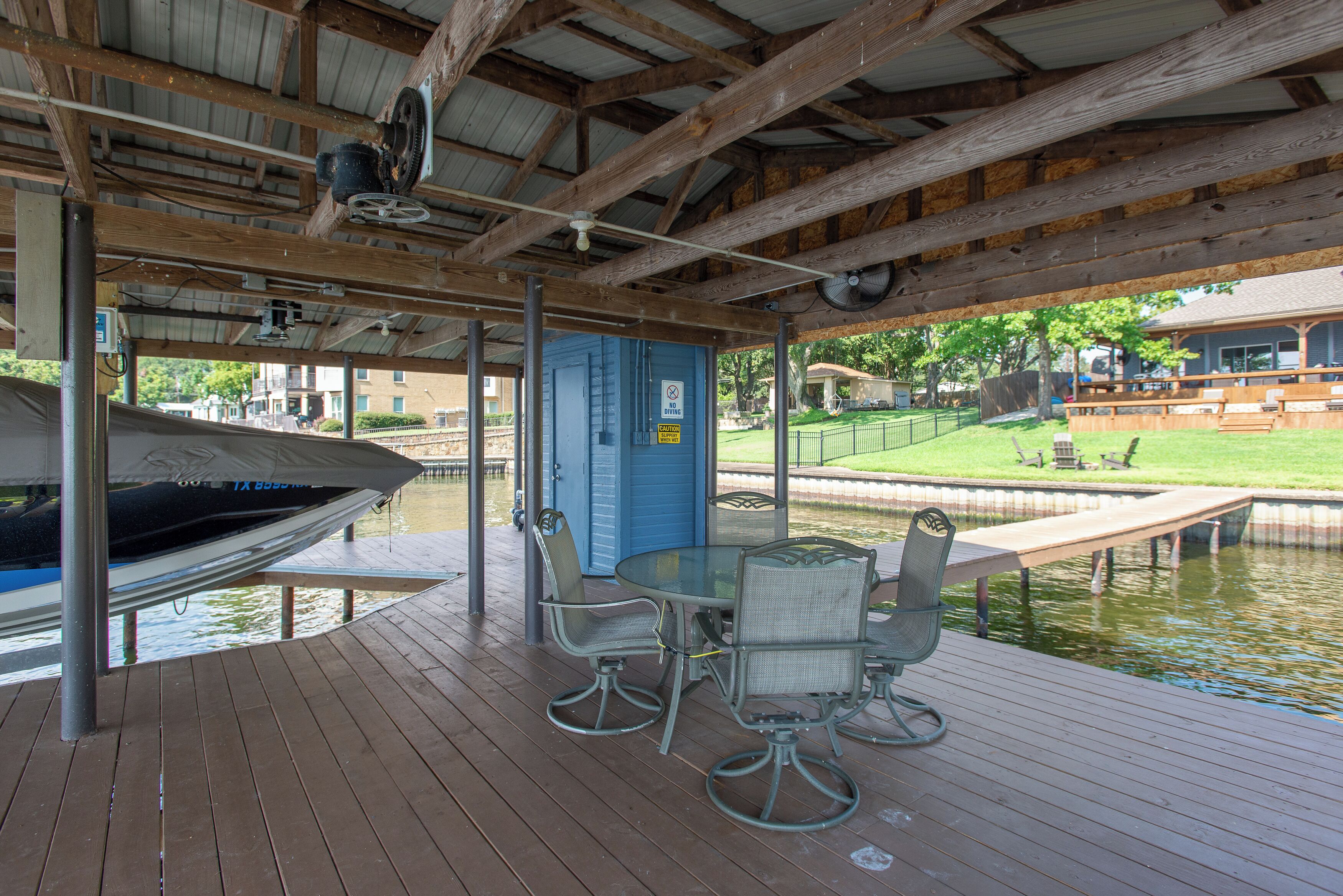 Un espace extérieur abrité avec une table et des chaises, un quai avec un bateau, et un bâtiment avec une porte bleue.