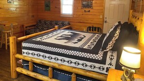 Une chambre aménagée dans un chalet en rondins, avec un lit, une chaise, une table et un ventilateur de plafond.