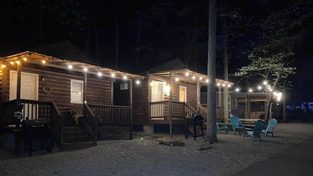 Une rangée de cabanes illuminées de guirlandes lumineuses, avec des espaces de repos en plein air et un chemin de gravier.