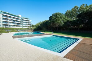 Een modern hotel met een zwembadgedeelte, inclusief twee zwembaden en een houten terras.