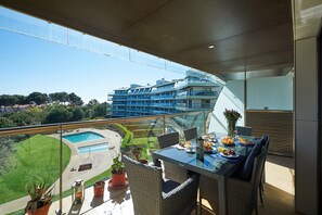 Een balkon met een eettafel, stoelen en uitzicht op een zwembad en gebouwen.