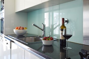 A modern kitchen with a stainless steel sink, a bowl of fruit, a bottle of wine, and a glass of wine on the counter.