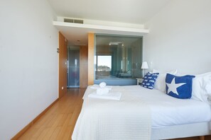 A hotel room with a large bed, a bathroom visible through a glass door, and a view of the outdoors.