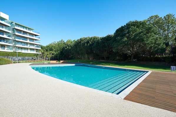 A swimming pool with a wooden deck, surrounded by a well-maintained lawn and trees.