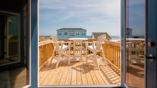 Een houten terras met een tafel en stoelen, met uitzicht op een strand met huizen.