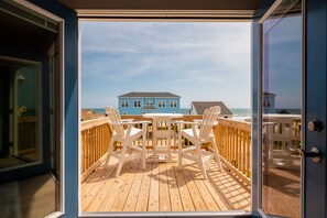 A wooden deck with a table and chairs, overlooking a beach with houses.
