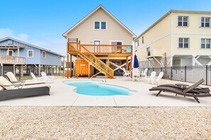 A pool area with lounge chairs, a wooden deck, and a two-story building with a balcony.