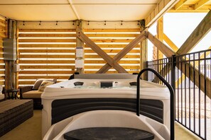 A hot tub in a wooden cabin with a view of a wooden deck and a staircase.