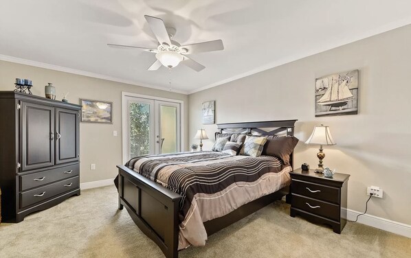 Een slaapkamer met een bed, nachtkastje, dressoir, plafondventilator en raam.