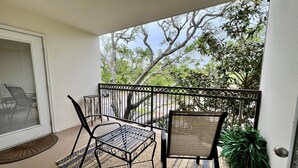 A balcony with a table and chairs, a metal railing, and a view of trees and sky. - Seaside Treasure - Beach, Pool, Casino, Family Activities, Sunsets, Relax. (Biloxi)
