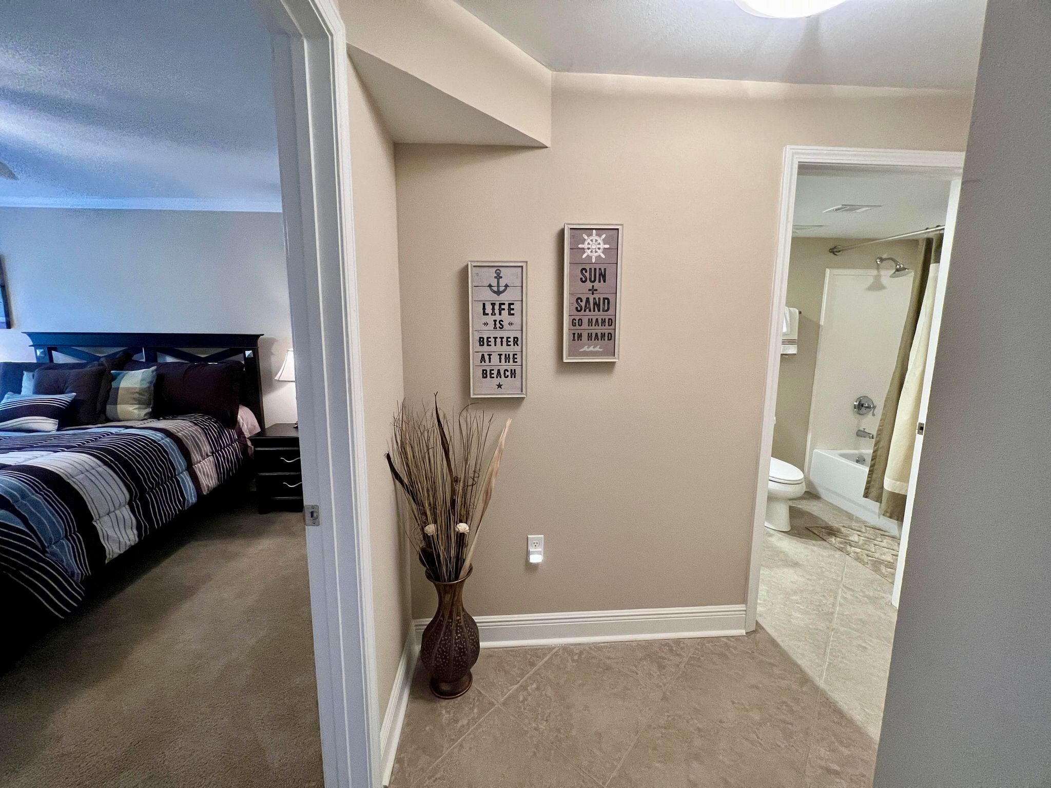 A bedroom with a bed, bedside table, and a nightstand. There is a bathroom visible with a shower, toilet, and sink.