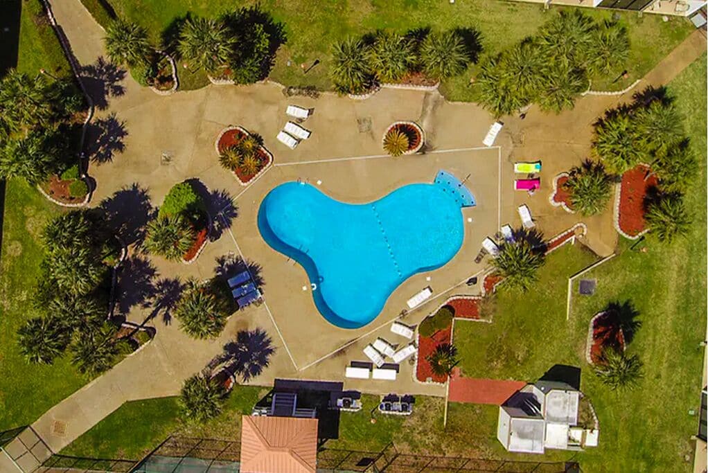 An aerial view of a property with a large swimming pool, surrounded by landscaped areas and a few buildings.