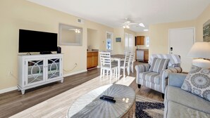 A living room with a television, a dining area with a table and chairs, a kitchen area, and a ceiling fan. - 8B Lighthouse Point Beach Club (Tybee Island)