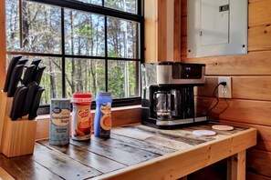 A kitchen with a coffee maker, a knife block, and two beverage cans on a wooden countertop. - Ellijay Cabin Getaway: Mountain Views, Fireplace & BBQ (Ellijay)