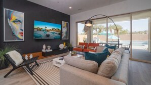 A modern living room with a large TV, comfortable seating, and a view of the outdoors.