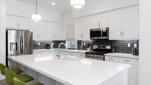 A modern kitchen with white cabinets, a large island, stainless steel appliances, and green chairs.