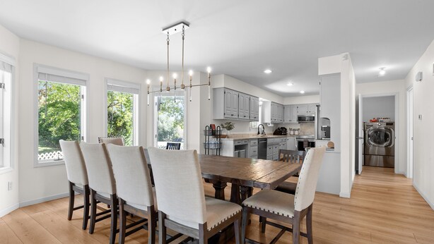 A modern kitchen with white cabinets, a wooden dining table, and a chandelier. - Spacious KC Home - Pickleball, Mini Golf, Gym, Luxurious Bathrooms, Swim Spa (Bonner Springs)