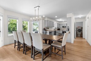 A modern kitchen with white cabinets, a wooden dining table, and a chandelier. - Spacious KC Home - Pickleball, Mini Golf, Gym, Luxurious Bathrooms, Swim Spa (Bonner Springs)
