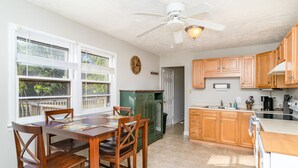 A kitchen with wooden cabinets, a dining table with chairs, a ceiling fan, and a view of the outdoors through large windows. - 3 BR Family Friendly Rambler (Hope Mills)