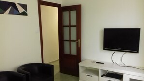A room with a television mounted on the wall, a white entertainment unit with drawers, two black chairs, and a wooden door with glass panels. - VoT Rupurupay B (Aldeadávila de la Ribera)