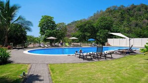 A swimming pool with lounge chairs and umbrellas, surrounded by greenery and a hilly landscape. - 7th Floor Direct Ocean View Penthouse -Parties OK. (Jacó)