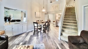 Een ruime woonkamer met een eettafel, een trap en een keuken met witte kasten.