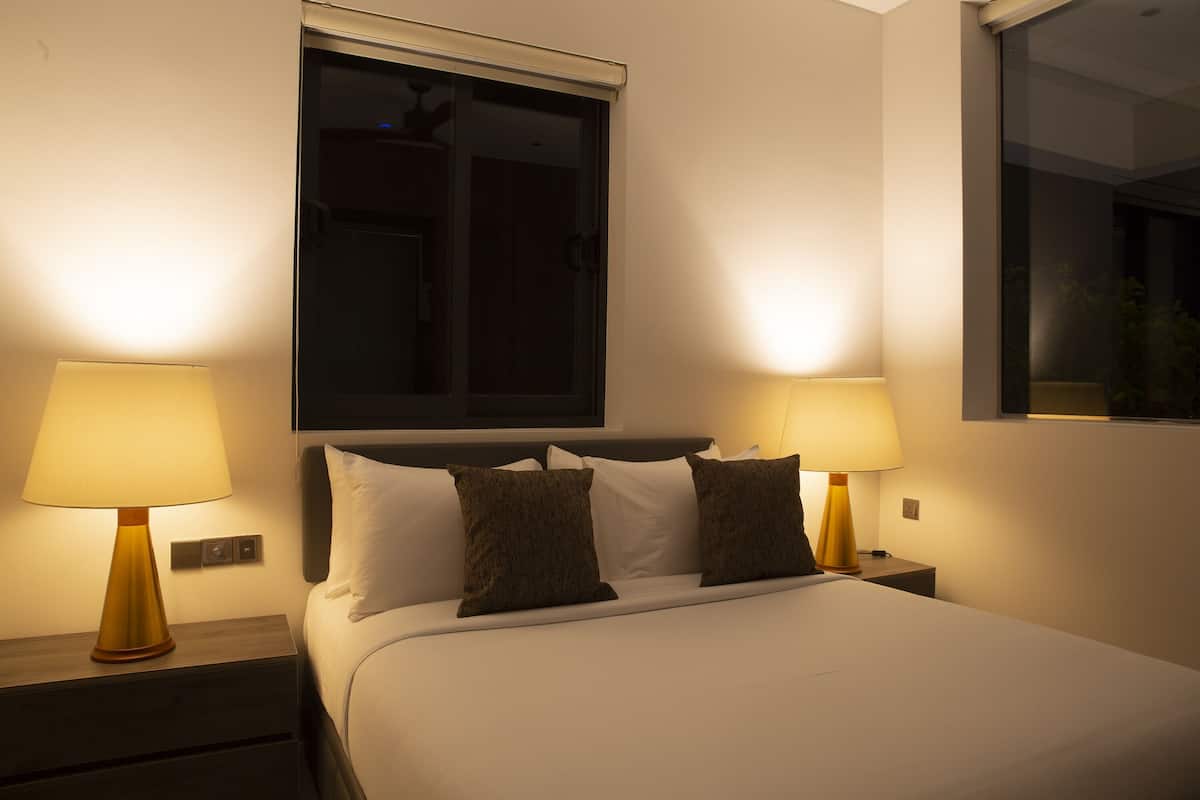 Una habitación de hotel con cama, dos lámparas de noche, una ventana y una mesita de noche.
