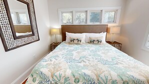 Une chambre à coucher avec un lit, deux lampes de chevet, un miroir et une fenêtre donnant sur des arbres.