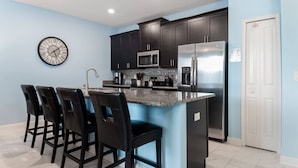 A modern kitchen with dark cabinets, a stainless steel refrigerator, a microwave, and a clock on the wall. - Family-Friendly 4BR Home w/ Pool, Resort Perks, & Disney Nearby (Kissimmee)