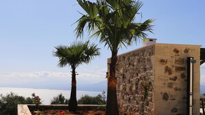 A stone building with a palm tree in front, a stone wall, and a view of the sea. - Villa Lisaya, a haven of peace with sea view and swimming pool, in a Natura 2000 area! (PALELONI)