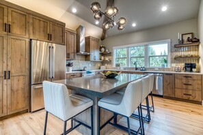 Une cuisine moderne avec des meubles en bois, des appareils électroménagers en acier inoxydable, un îlot central doté de tabourets de bar et une grande fenêtre qui laisse entrer la lumière naturelle.