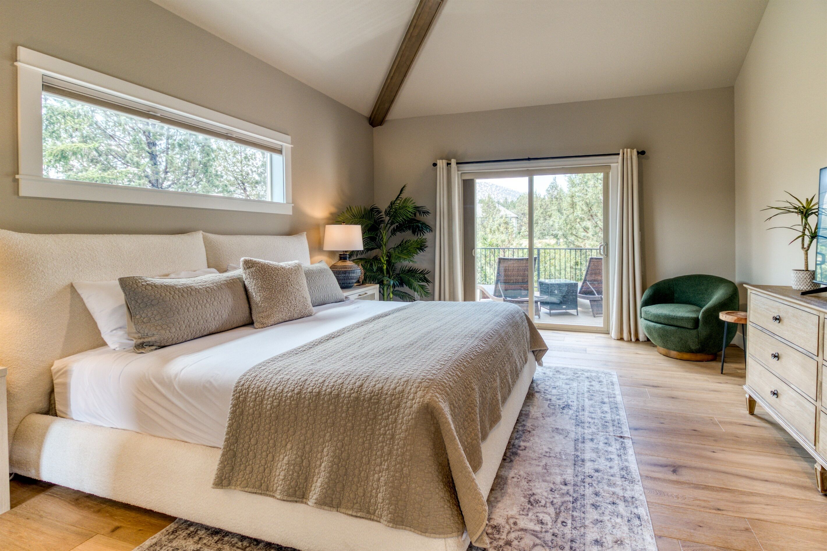 A bedroom with a large bed, a nightstand, a lamp, a green chair, a dresser, and a sliding glass door leading to a balcony.