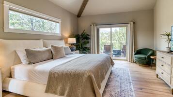A bedroom with a large bed, a nightstand, a lamp, a green chair, a dresser, and a sliding glass door leading to a balcony.