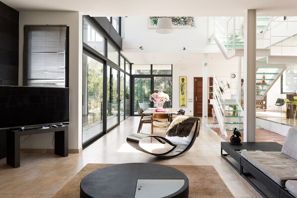 A spacious living area with a large TV, a dining table, and a comfortable seating area with a sofa and chairs.