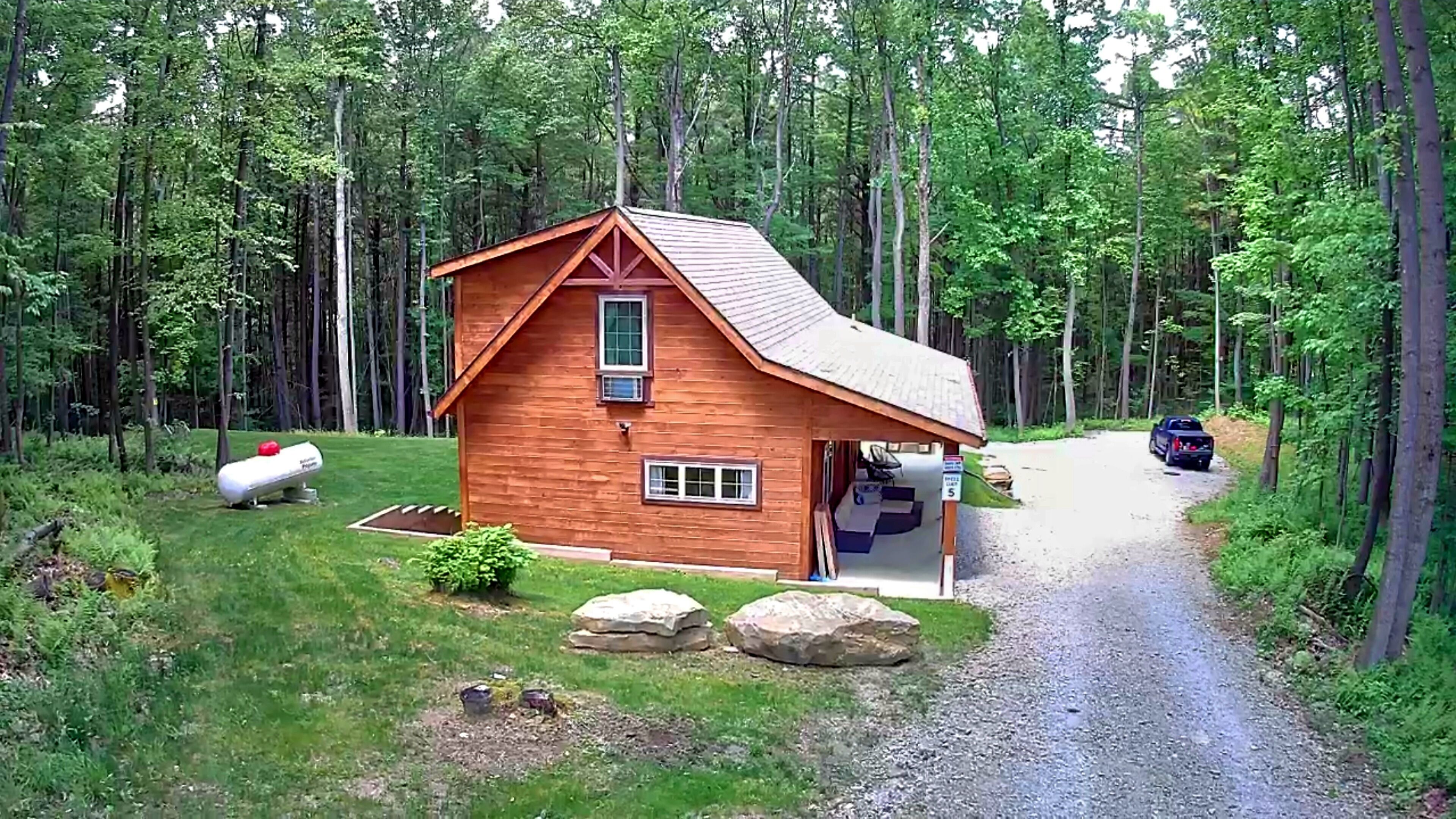 Une cabane en bois avec une allée en gravier, entourée d’une forêt.