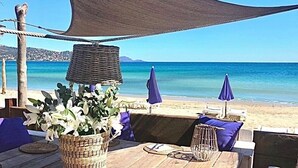 A beachside seating area with wicker furniture, a table with a placemat, and a large shade sail.