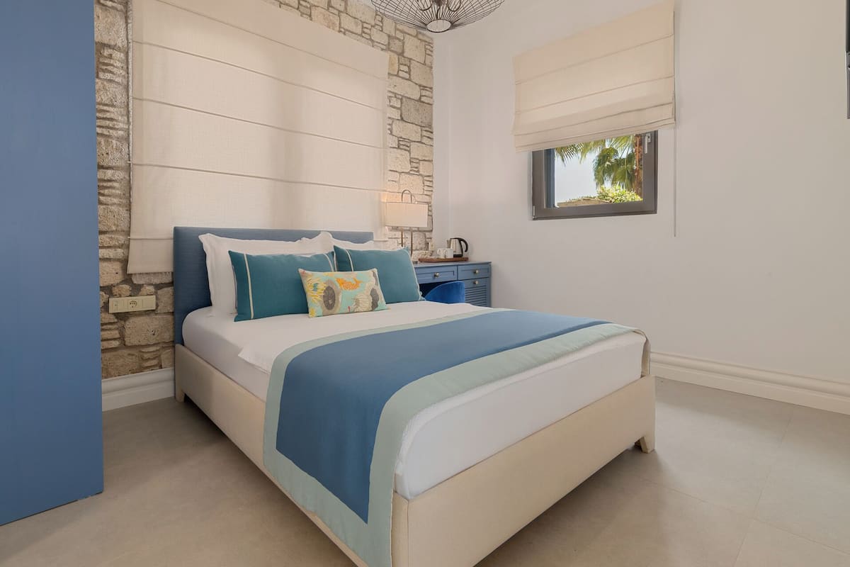 A bedroom with a bed, a nightstand, a lamp, and a window with a view of greenery.