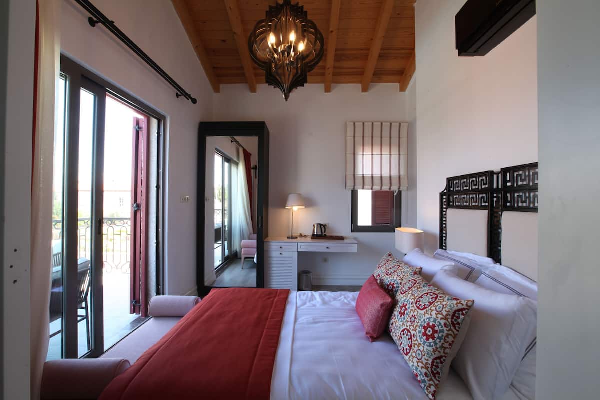 A bedroom with a bed, a desk, a chair, a lamp, and a window.