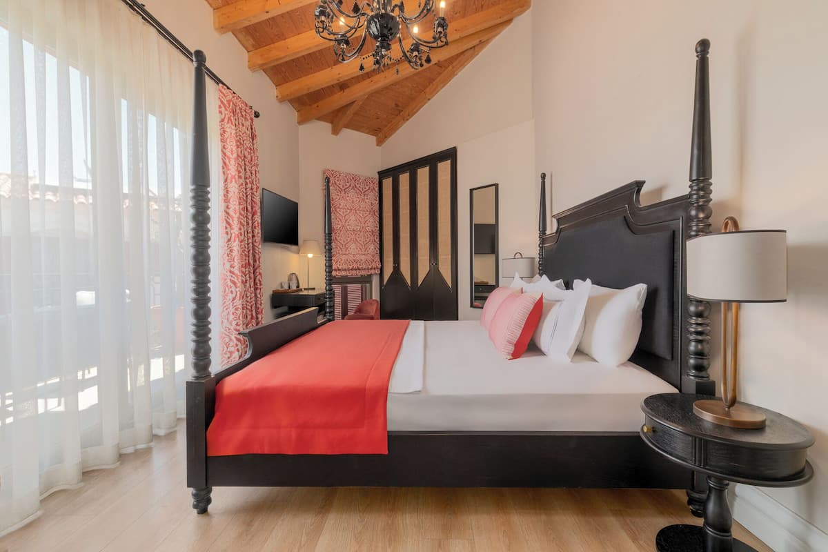 A bedroom with a wooden ceiling, a four-poster bed, a TV, and a bedside table with a lamp.