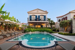 A pool area with lounge chairs, a pool, and a two-story building with balconies.