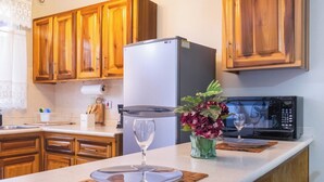 Une cuisine avec des meubles en bois, un réfrigérateur, un four à micro-ondes et un coin repas avec une assiette et un verre.
