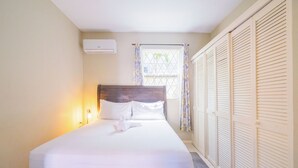 Un lit bien fait, avec du linge de lit blanc, une tête de lit en bois et une lampe de chevet.