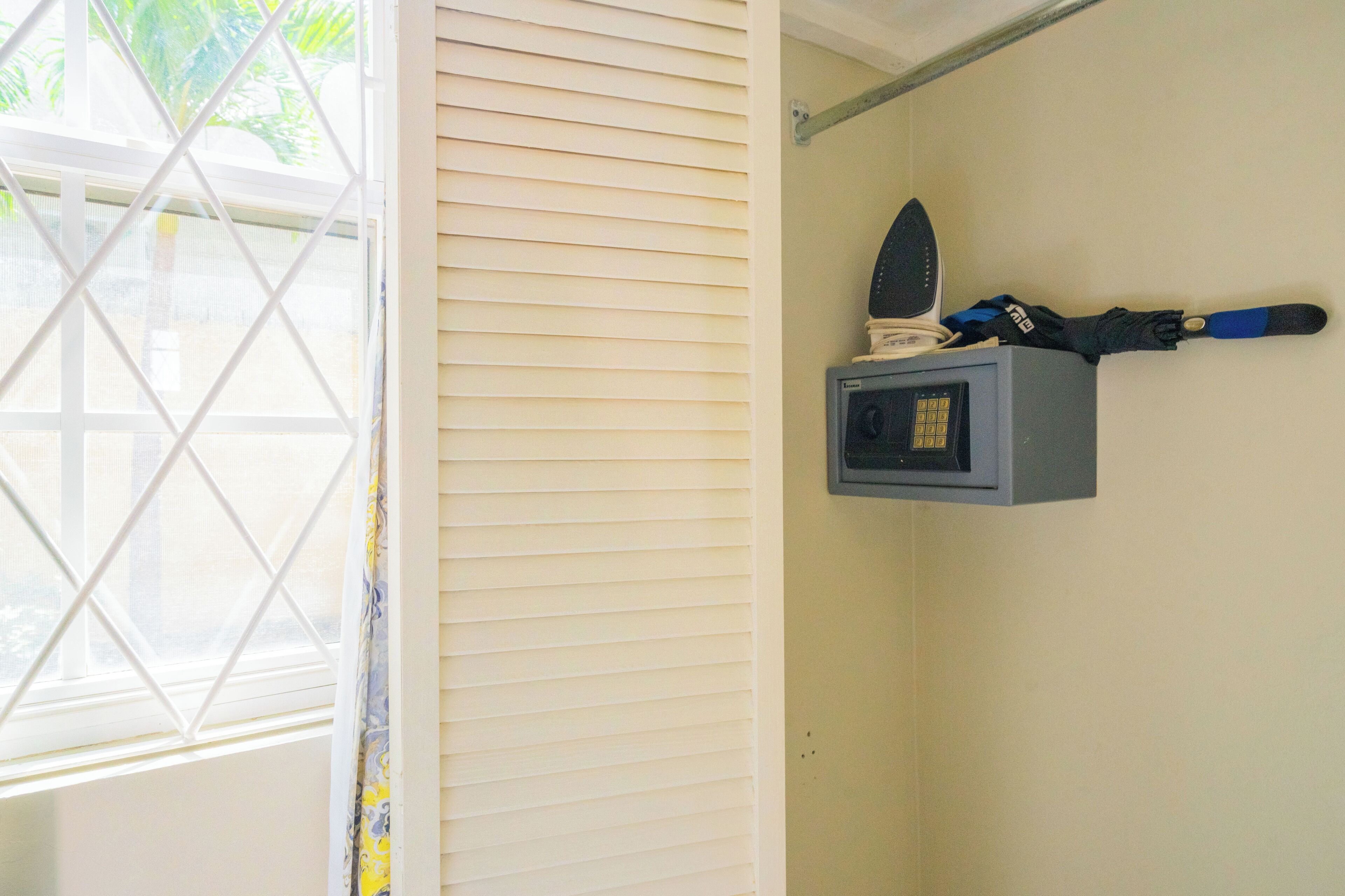 Una habitación con ventana, una tabla de planchar en la pared y un pequeño electrodoméstico.