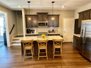 Una cocina moderna con armarios de madera oscura, electrodomésticos de acero inoxidable y una isla central con taburetes de bar.