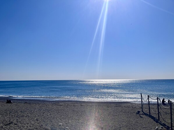A beach with a clear sky, calm sea, and a sun shining.